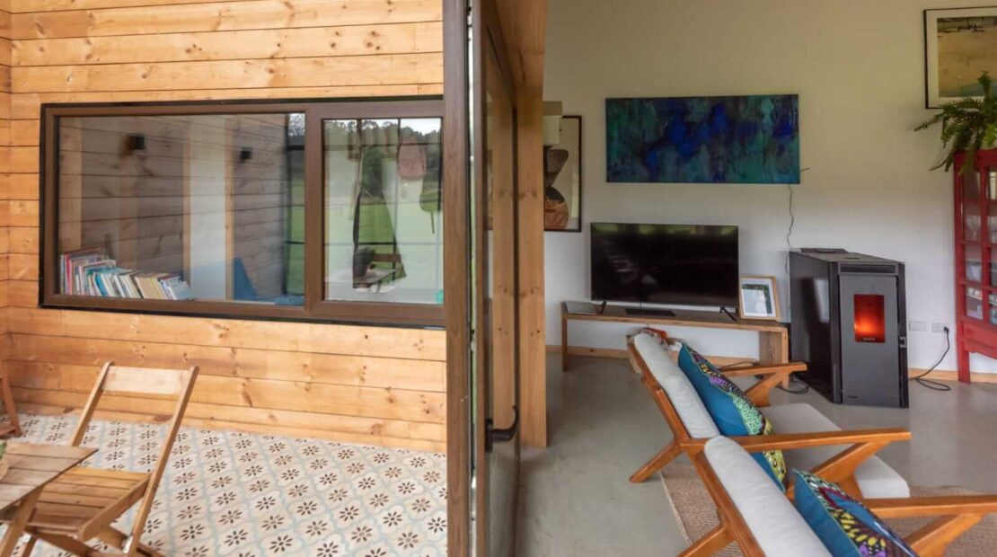 Interior de casa moderna en el sur de Chile con estufa a pellet, mobiliario de madera y ventanales hacia la naturaleza