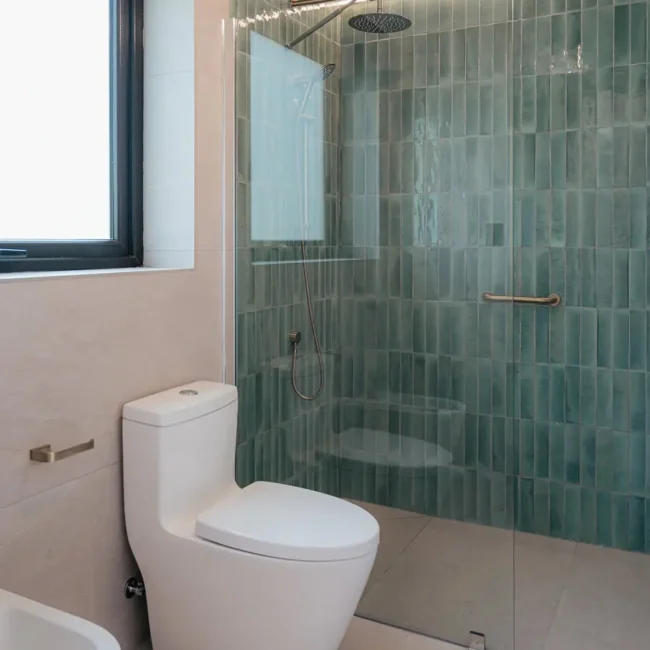 Baño de Casa DLM con cerámica verde, madera y terminaciones interiores