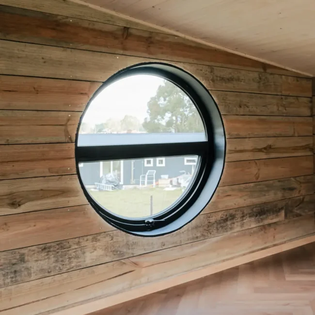 Detalle de ventana circular y revestimiento de madera en Casa DLM